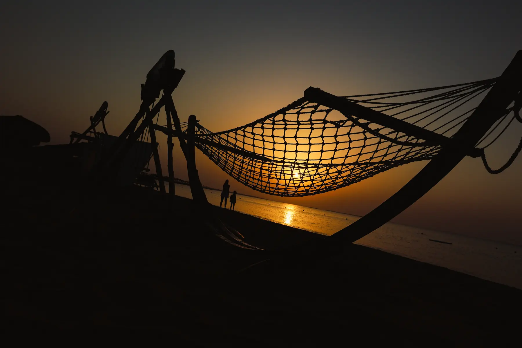 Beach hammock at sunrise with guests walking along the Red Sea shoreline at Caribbean World Resorts Hurghada