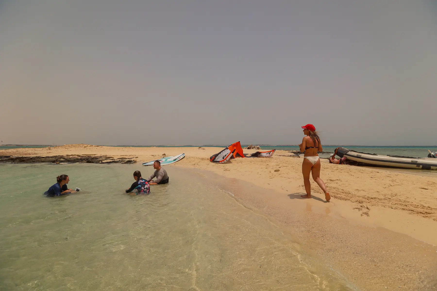 Three people sitting in shallow Red Sea water on a sandbank near Caribbean World Resorts Hurghada as a woman walks past, photographed by VirtuPeek